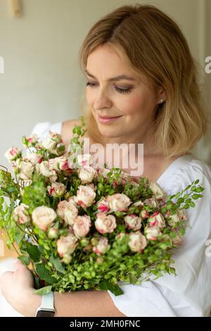 Una donna di mezza età sta in cucina con un bouquet di flusso Foto Stock