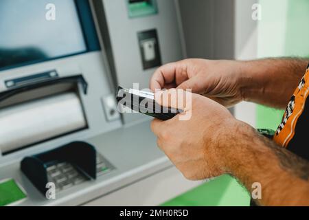 Carta bancomat MAN. Scheda di inserimento ATM. Uomo che mette la carta di credito in bancomat mentre tiene il portafoglio Foto Stock