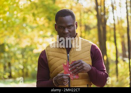 Ritratto l'uomo afroamericano triste o arrabbiato tiene foglia d'acero autunnale. Autunno natura. Moda autunnale stagionale e cattiva emozione. Foto Stock