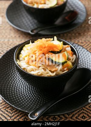 Zuppa asiatica con tagliatelle di mirne, TVP, cavolo, zucchine e carote grattugiate. Foto Stock