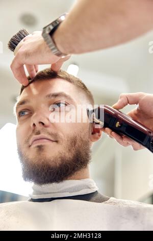 Parrucchiere con rifinitore su bell'uomo bearded Foto Stock