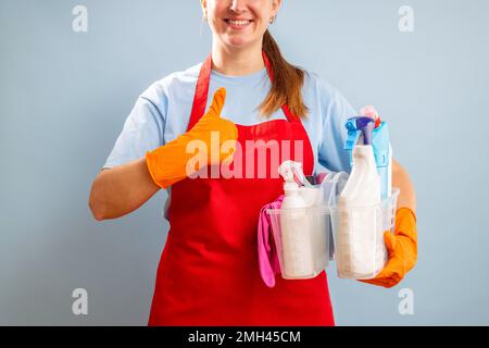 Donna in guanti e grembiule che regge cestello con spugna e prodotti per la pulizia Foto Stock