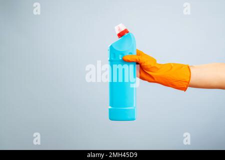 Mano nel guanto contenente una bottiglia di detergente in plastica su sfondo blu Foto Stock