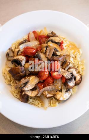 Friggere verdure, pomodori ciliegini, funghi e cipolla serviti con tagliatelle Raman condite. Foto Stock