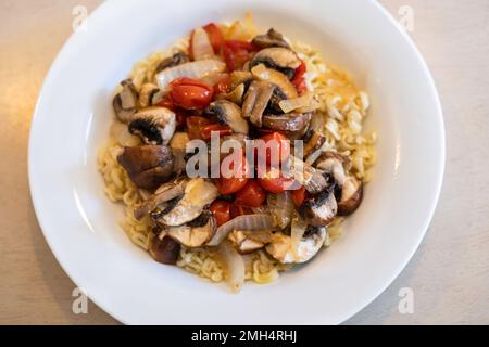 Friggere verdure, pomodori ciliegini, funghi e cipolla serviti con tagliatelle Raman condite. Foto Stock