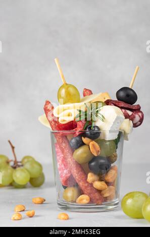 Jarcuterie in un bicchiere comprende vari tipi di salsicce, sottaceti, formaggi, noci, verdure e frutta. Versione moderna di spuntino festivo Foto Stock