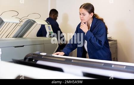 Donna che lavora in una stampa e stampa verifica la qualità di stampa al centro della stampante Foto Stock