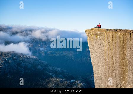 Preikestolen - incredibile roccia in Norvegia. Ragazzo su una scogliera sopra le nuvole. Pulpit Rock, la più famosa attrazione turistica di Ryfylke, domina il Ly Foto Stock