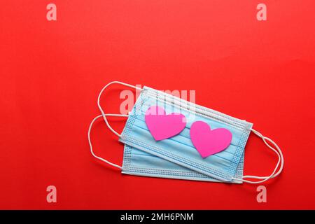 Maschera di protezione a tre strati per uso clinico con cuori rosa su sfondo rosso Foto Stock