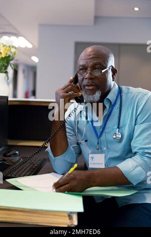 Medico afro-americano che lavora in ospedale, parlando al telefono Foto Stock