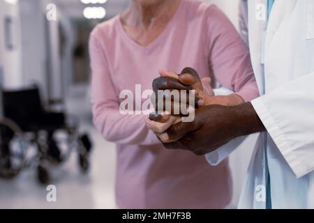 Primo piano del medico afro-americano e del paziente caucasico senior che tiene le mani Foto Stock