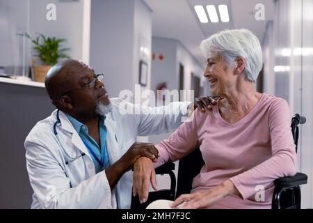 Medico afro-americano che parla con un paziente caucasico anziano seduto in sedia a rotelle Foto Stock