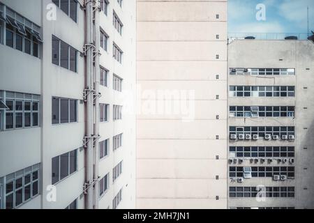 Una vista grandangolare di un angolo interno di due edifici con molte finestre, aria condizionata esterna su una facciata intonacata, e tubi su un sole Foto Stock