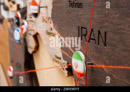 La bandiera iraniana sul puntello con filo rosso ha mostrato i percorsi di movimento o le aree di influenza nell'economia globale sulla mappa di legno. Pianificazione del viaggio o concetto logistico. Collegamento di reti secondo il concetto di sanzioni. Foto Stock
