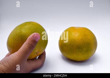 Una mano raccoglie un arancione su uno sfondo bianco. Foto Stock