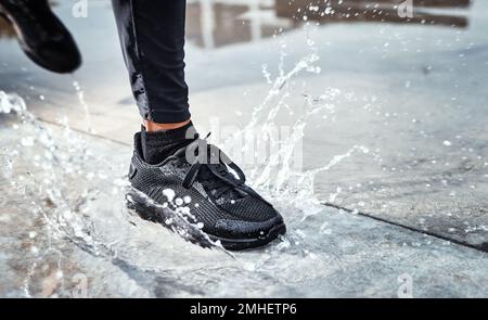 I piedi spruzzano l'acqua in strada, la persona che corre sotto la pioggia e le scarpe in pozzanghera di Seattle Road per il cardio all'aperto. Allenamento per i corridori per la maratona, continua Foto Stock