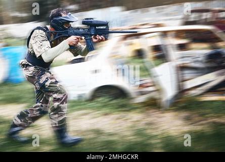 Paintball, mira e uomo con una pistola per un gioco con movimento sfocato in un'arena o campo all'aperto. Sfida, competizione e soldato maschile con un mimetizzazione Foto Stock