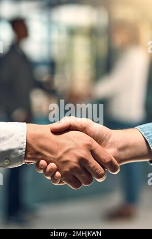 Per vincere. due giovani partner aziendali non identificabili che si stringono le mani in ufficio. Foto Stock