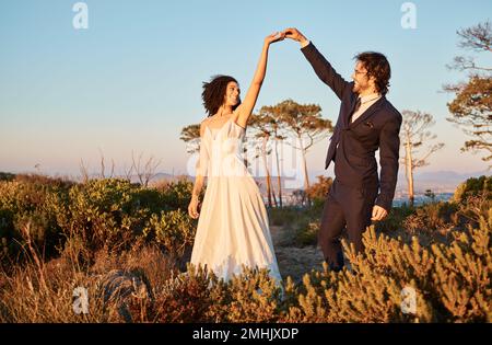 Amore, matrimonio e tenere mani per la danza con la coppia nel parco naturale per la celebrazione, romanticismo e felicità. Tramonto, sostegno ed estate con sposa e. Foto Stock