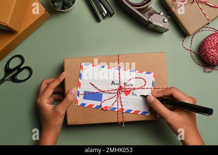 Vista dall'alto del biglietto d'auguri firmato da donna, circondato da materiali da imballaggio regalo. Preparazione per il concetto di vacanza Foto Stock