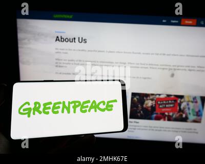 Persona che tiene il telefono cellulare con il logo della campagna ambientale rete Greenpeace sullo schermo di fronte alla pagina web. Messa a fuoco sul display del telefono. Foto Stock