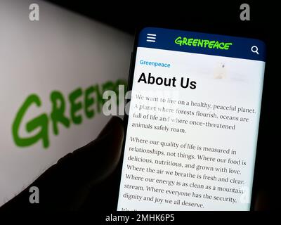 Persona che tiene il cellulare con pagina web di campagna ambientale rete Greenpeace sullo schermo con logo. Messa a fuoco al centro del display del telefono. Foto Stock