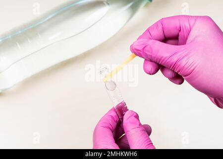 la mano con guanti può contenere carta al tornasole neutra su una provetta e un campione di acqua potabile naturale sul flacone su una scrivania leggera Foto Stock