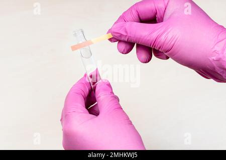 mani che tengono il test al tornasole di acido rosa e la provetta su un tavolo leggero Foto Stock