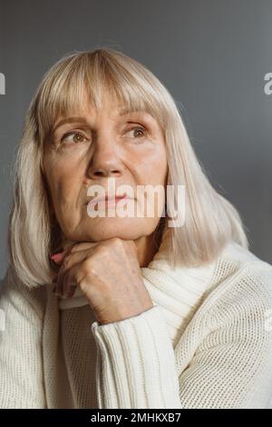 Ritratto di una donna anziana di mezza età che si rilassa su un comodo divano, godendo di un momento di pace all'interno. Foto Stock