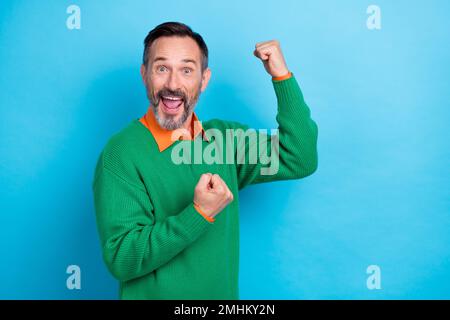 Foto ritratto di maturo bel mister sollevare pugni celebrare promozione lotteria vestito elegante aspetto verde isolato su sfondo di colore blu Foto Stock