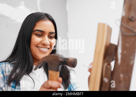 Una giovane donna indiana attraente martella un chiodo in casa di legno fai da te Foto Stock