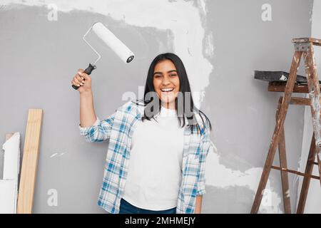 La giovane donna indiana si posa con il rullo del pennello che si prepara a dipingere il muro Foto Stock