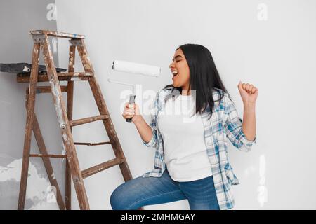 Primo piano ripresa di una giovane donna che cantava e ballava mentre dipingi il muro di casa fai da te Foto Stock