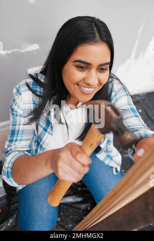 Una giovane donna indiana attraente martella un chiodo in casa di legno fai da te Foto Stock