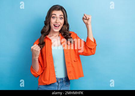 Foto di adorabile bello carino donna brunette capelli ricci sollevare pugni celebrare il suo lavoro di approvazione isolato su sfondo di colore blu Foto Stock