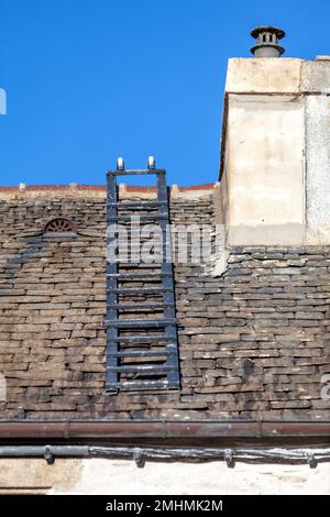 Scala del tetto su un vecchio tetto in ardesia durante la riparazione di un camino lampeggiante. Foto Stock