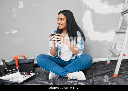 Una giovane donna indiana attraente siede sul pavimento prendendo il caffè pausa dal fai da te Foto Stock