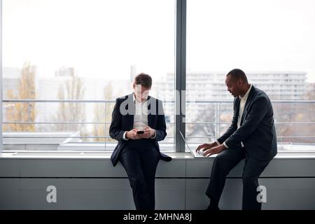 Uomini d'affari che utilizzano il telefono e il computer portatile in ufficio Foto Stock