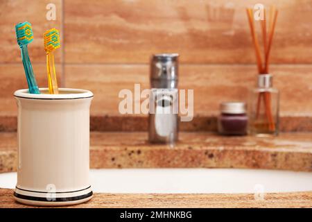 La tazza con gli spazzolini colorati sul lavabo nel bagno. Assistenza sanitaria, routine mattutina e sfondo igienico Foto Stock