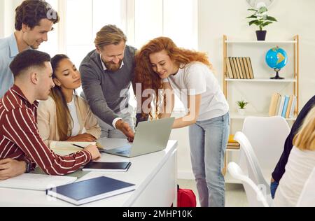 Il professore e gli studenti stanno lavorando al progetto sul laptop insieme seduti alla scrivania e in piedi vicino. Foto Stock