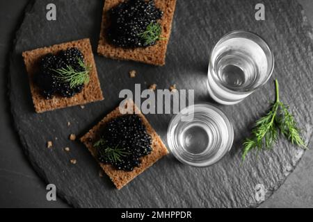 Vodka russa fredda con spuntini su tavola nera, piatto Foto Stock