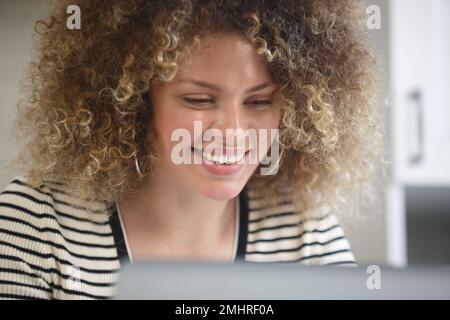 Felice donna riccio lavora sul computer a casa. Ritratto di allegra donna bianca che fa lavoro a distanza online con un computer portatile Foto Stock