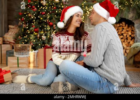 Felice giovane coppia indossando cappelli Santa in soggiorno decorato per Natale Foto Stock