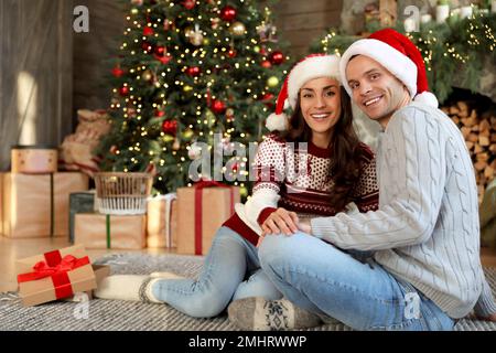 Felice giovane coppia indossando cappelli Santa in soggiorno decorato per Natale Foto Stock