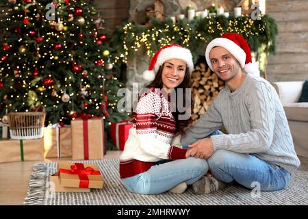 Felice giovane coppia indossando cappelli Santa in soggiorno decorato per Natale Foto Stock