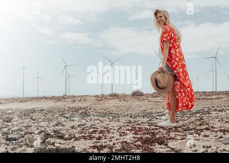 Giovane ragazza bionda che posa in un campo asciutto con alcune turbine eoliche sullo sfondo. Foto Stock