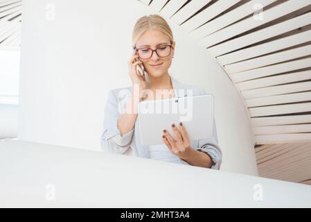 Giovane donna occupata a parlare al telefono con un dispositivo bianco Foto Stock