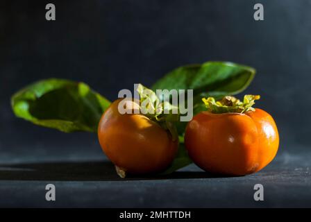 Persimmons maturo arancione pronto a mangiare su fondo scuro orizzontale Foto Stock