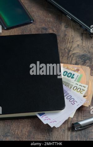 Frammento di libro contabile di un dispositivo di conto con banconote in euro e una penna stilografica sullo sfondo di un tavolo di legno. Foto Stock