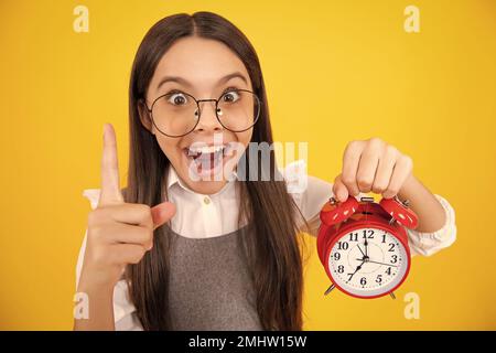 Ritratto di ragazza adolescente con orologio alrm, tempo e scadenza. Studio shot isolato su sfondo giallo. Ragazza giovane sorpresa. Foto Stock
